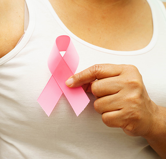 A person wearing a white shirt holds a pink ribbon to support breast health awareness.
