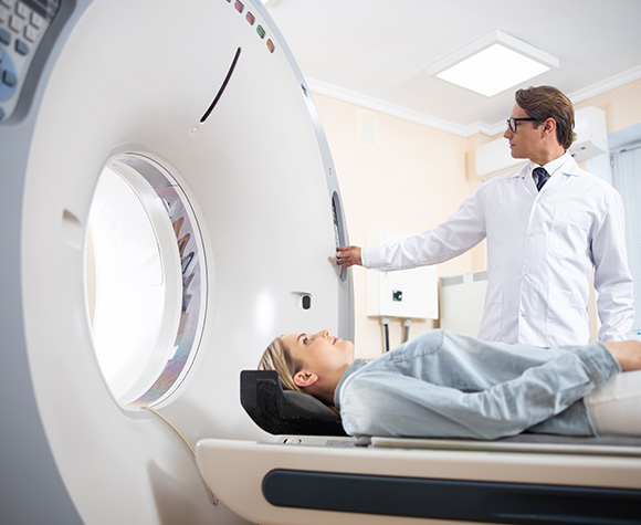 Radiologist operating a CT scanner while a patient lies on the examination bed.